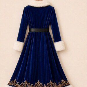 May include: A long-sleeved royal blue velvet coat featuring a white faux fur collar and cuffs. The coat includes a black belt at the waist and a gold-colored embroidered floral pattern along the bottom hem, which is also trimmed with white faux fur.