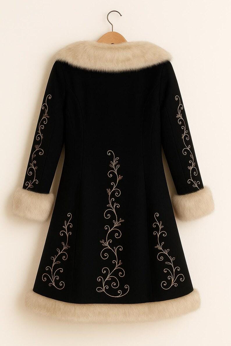 May include: A black coat featuring a beige faux fur collar, cuffs, and hem. The coat is decorated with light-colored, swirling floral embroidery patterns running down the center and along the length of each sleeve, hanging on a wooden hanger.