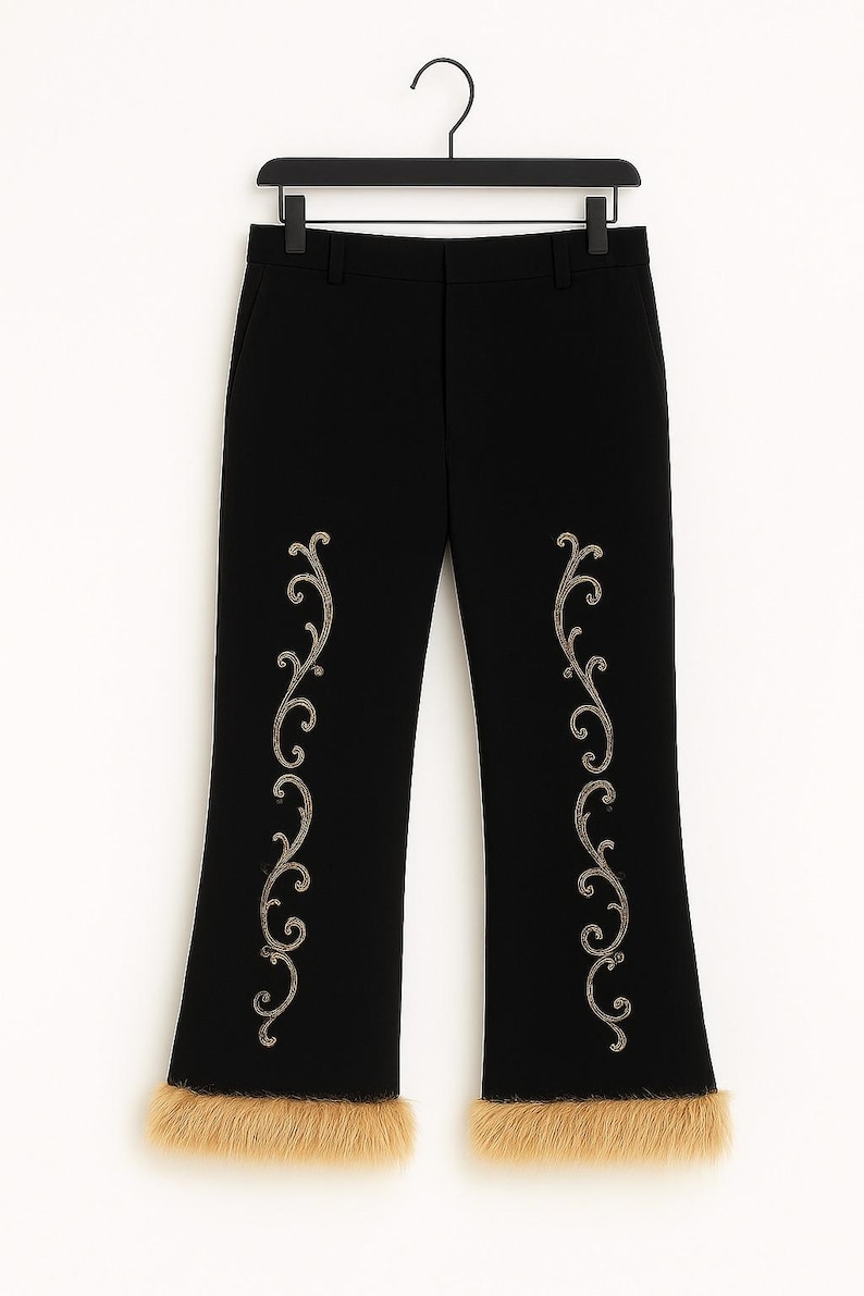 Pu&ograve; includere: Pantaloni neri caratterizzati da un motivo a volute ricamato color oro su ogni gamba e da un bordo in pelliccia sintetica color cuoio sull'orlo inferiore. I pantaloni sono appesi a una gruccia di plastica nera su sfondo bianco.