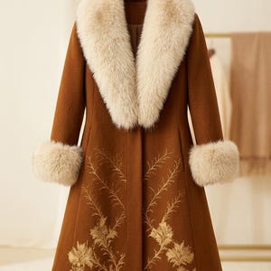 May include: A long brown coat featuring a large cream-colored faux fur collar and matching faux fur cuffs on the sleeves. The lower portion of the coat is decorated with intricate gold-toned embroidery depicting delicate floral and leaf patterns.