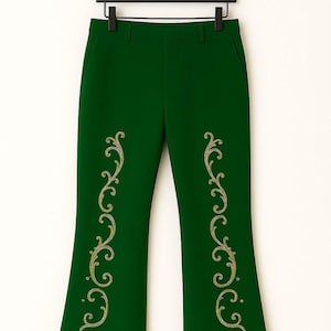 Pu&ograve; includere: Pantaloni verde scuro con motivi a volute dorate ricamati che corrono verticalmente sulla parte anteriore di ogni gamba. L'orlo di ogni gamba &egrave; rifinito con un bordo spesso in pelliccia sintetica color marrone chiaro. I pantaloni sono su una gruccia nera.