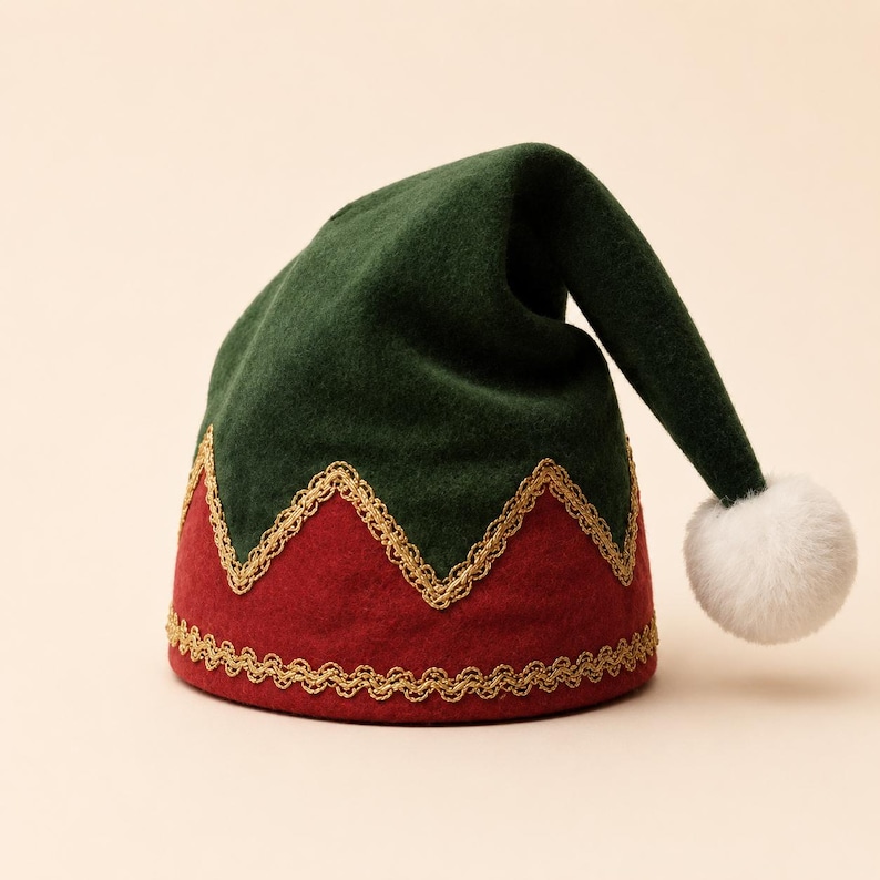 Puede incluir: Un gorro de fieltro verde oscuro y rojo con una parte superior puntiaguda y ca&iacute;da, rematado con un pomp&oacute;n blanco. El gorro presenta un borde met&aacute;lico dorado en la base y un patr&oacute;n en zigzag que separa las secciones verde y roja.