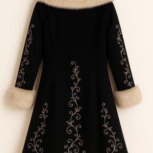 May include: A black coat featuring a beige faux fur collar, cuffs, and hem. The coat is decorated with light-colored, swirling floral embroidery patterns running down the center and along the length of each sleeve, hanging on a wooden hanger.