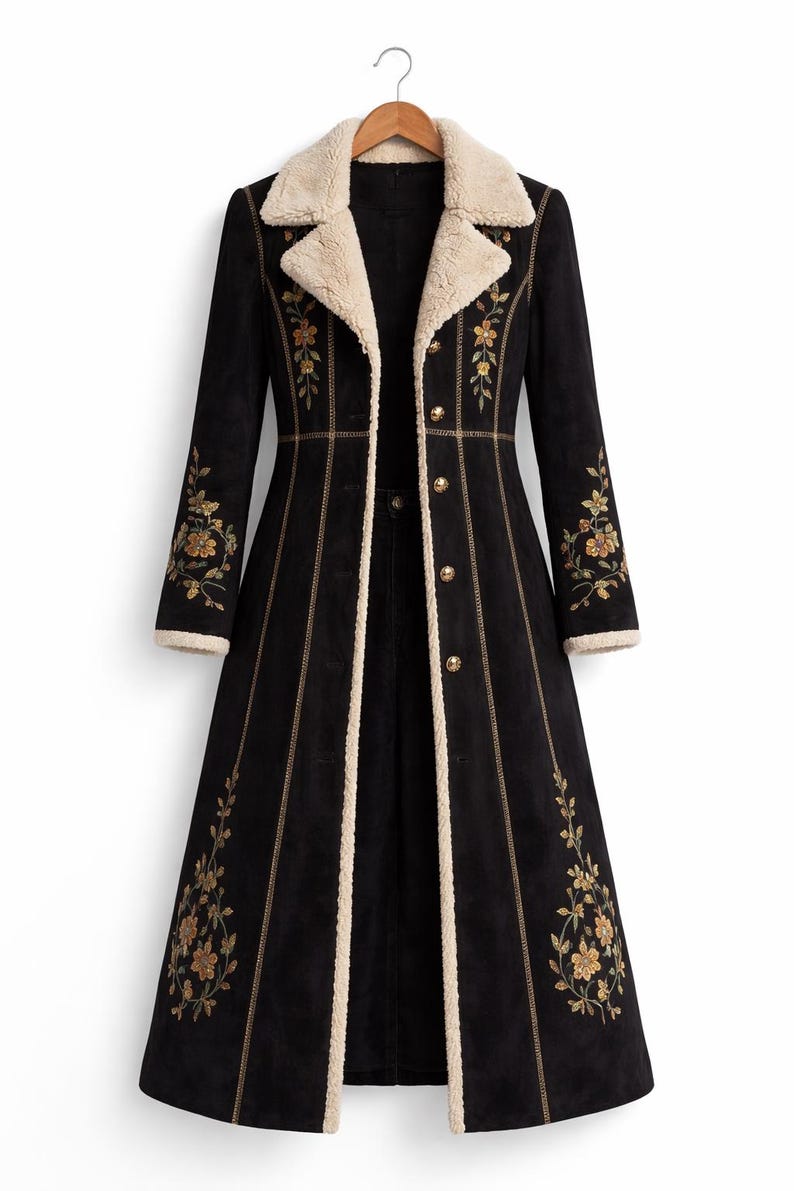 May include: A long black coat with a cream-coloured faux fur collar and trim. The coat features gold floral embroidery on the sleeves and front, with gold button closures. The coat is hanging on a wooden hanger.