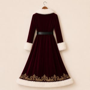 May include: A long-sleeved, floor-length burgundy velvet coat featuring a white faux fur collar and matching white faux fur cuffs. The coat includes a black belt at the waist and a gold embroidered scroll pattern along the bottom hemline.