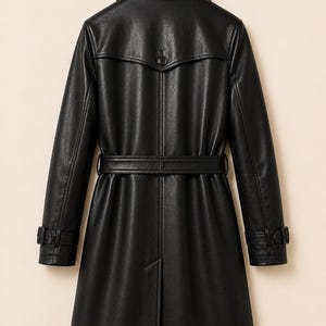 May include: A black trench coat featuring a collared neckline, long sleeves with buckled cuffs, a belted waist, and a back storm flap with a single button. The coat has a smooth, textured finish and a central vertical seam extending to the hem.