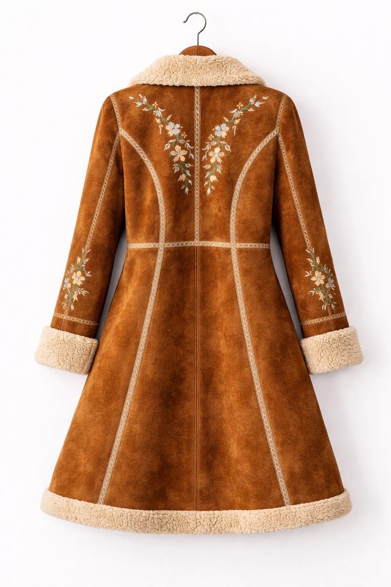 May include: A long brown coat featuring a cream-colored faux shearling collar, cuffs, and hem. The coat is decorated with floral embroidery on the upper back and sleeves, accented by light-colored vertical piping along the seams and a flared cut.