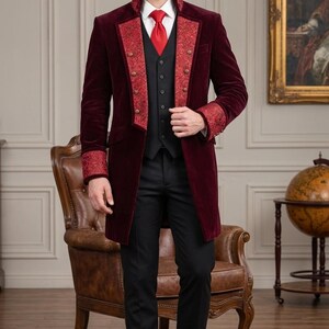 Puede incluir: Una levita de terciopelo burdeos con solapas y pu&ntilde;os de estampado rojo, sobre un chaleco negro, camisa blanca de cuello, corbata roja y pantal&oacute;n negro. El abrigo presenta botones de tono dorado en la parte delantera y un cuello alto.