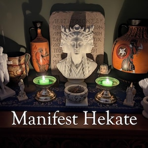 May include: A white three-faced bust of Hekate centered before a stone tablet with Greek text. Flanking the bust are two orange and black ceramic vases, two green tea light candles in silver holders, small white statues, and a mortar and pestle.