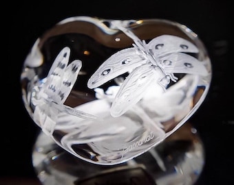Könnte beinhalten: Eine klare, herzförmige Kristallskulptur mit einem geätzten Libellen-Design. Die Libelle hat detaillierte Flügel und Körper. Die Skulptur ist transparent, mit dem Wort "Baccarat" auf der Seite geätzt. Der Hintergrund ist dunkel.
