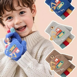 May include: Three pairs of children's convertible mittens in blue, gray, and brown. Each mitten features a cartoon excavator design and the text "Cool Boy." The mittens have a button closure and colorful striped cuffs.