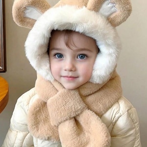 May include: A child wearing a beige faux fur hood with bear ears and a matching scarf. The hood has a white faux fur trim around the face. The child is wearing a quilted jacket.
