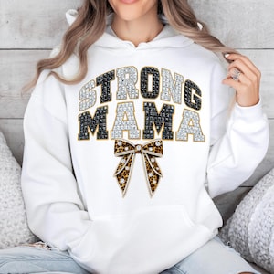 Puede incluir: Sudadera con capucha blanca con el texto "STRONG MAMA" en un diseño de joyas. La palabra "STRONG" está en negro y plata, y "MAMA" está en negro y plata. Un lazo con estampado de leopardo está debajo.