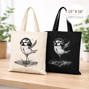 Peut inclure: Deux sacs fourre-tout, un crème et un noir, chacun avec une illustration détaillée d'un oiseau portant un casque et dansant dans l'eau. Les sacs mesurent 38 cm x 41 cm et sont en 100 % coton.