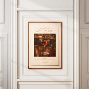 May include: A framed print featuring a Manhattan cocktail recipe. The print has a brown wooden frame and a cream-colored background. The image shows a cocktail in a stemmed glass with a cherry garnish. The text "MANHATTAN" is at the top.