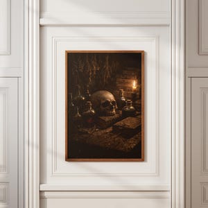 May include: A framed print featuring a still life with a human skull, glass bottles, and books. A lit candle provides the only light source, casting shadows on the objects. The artwork has a dark, gothic theme.
