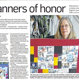 Op de afbeelding: Een vrouw houdt een rood, wit en geel quilt met kleine vierkanten met foto's van militair personeel. De quilt is een herdenkingsvlag voor de ouders van gesneuvelde militairen. De tekst "Long May It Wave" is zichtbaar op de quilt.