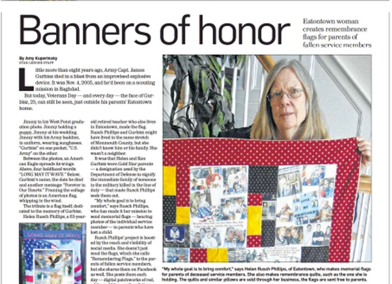 Op de afbeelding: Een vrouw houdt een rood, wit en geel quilt met kleine vierkanten met foto's van militair personeel. De quilt is een herdenkingsvlag voor de ouders van gesneuvelde militairen. De tekst "Long May It Wave" is zichtbaar op de quilt.