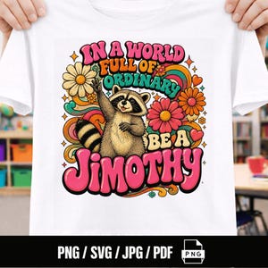 Könnte beinhalten: Ein weißes T-Shirt mit einer bunten Grafik eines winkenden Waschbären, umgeben von Blumen, Wirbeln und Herzen im Retro-Stil. Der Text lautet: IN A WORLD FULL OF ORDINARY BE A JIMOTHY. Das Design verwendet eine lebendige Palette aus Pink, Orange und Türkis.