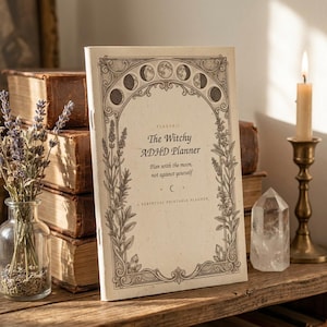 Può includere: Un'agenda color crema intitolata The Witchy ADHD Planner con il sottotitolo Plan with the moon, not against yourself. La copertina presenta un'illustrazione di bordo botanico e fasi lunari marrone scuro con rametti di lavanda e cristalli.