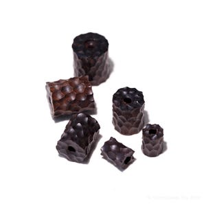 May include: A collection of dark brown wooden beads with a textured, geometric pattern. The beads vary in size and shape, including cylindrical and rectangular forms, each with a central hole for stringing. The beads are displayed against a white background.