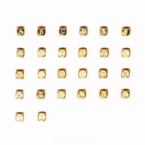 Op de afbeelding: Gouden alfabetkralen, elk met een letter van A tot Z, op een witte achtergrond. De vierkante kralen hebben een metallic afwerking. Ideaal voor het maken van sieraden en knutselprojecten.