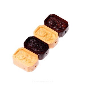 May include: Four rectangular wooden beads with carved rose designs. The beads are in varying shades of brown and tan, with a hole drilled through each for stringing. The rose carvings are detailed and prominent.