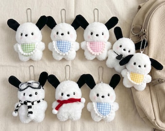 Può includere: Una collezione di otto portachiavi in peluche a forma di cane bianco con orecchie nere. Alcuni indossano bavaglini a quadretti verdi, blu, rosa o gialli, mentre altri presentano accessori come una sciarpa a righe con occhiali o una sciarpa rossa.