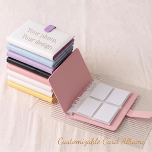 May include: A stack of six small, rectangular, multi-colored card albums with a white top cover featuring the text Your photo, Your design. One open pink album lies flat, revealing a white ring-bound interior with four empty card slots.