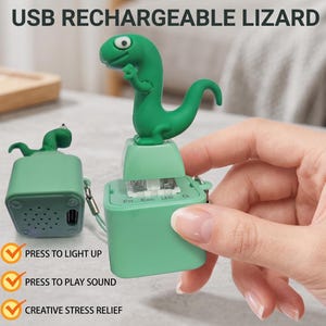 Könnte beinhalten: Ein grünes, per USB aufladbares Echsenspielzeug mit einer kleinen grünen Echsenfigur. Das Spielzeug hat Knöpfe mit den Bezeichnungen Fn, Esc und LED. Der Text lautet "PRESS TO LIGHT UP", "PRESS TO PLAY SOUND" und "CREATIVE STRESS RELIEF".