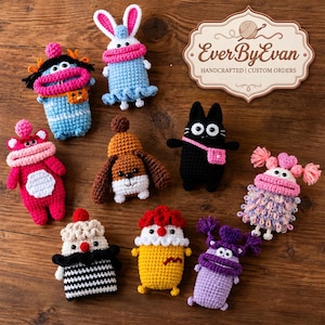 Op de afbeelding: Een verzameling van negen kleurrijke gehaakte knuffels met unieke kenmerken, waaronder een konijn, een zwarte kat en diverse figuren, naast een decoratief bord met EverByEvan HANDCRAFTED | CUSTOM ORDERS.