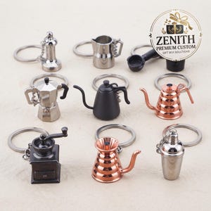 May include: A collection of nine miniature coffee-themed keychains featuring various designs including a silver tamper, a metal pitcher, a black portafilter, a moka pot, a black gooseneck kettle, a copper kettle, a coffee grinder, and a cocktail shaker.
