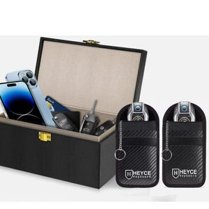 May include: Black box with a gold clasp, open to reveal a smartphone, keys, and a credit card. Two black key fob protectors with the text "HEYCE KeyGuard" are on the right.