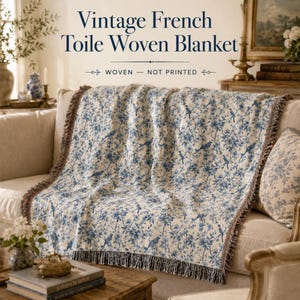 K&ouml;nnte beinhalten: Eine Vintage-Decke aus franz&ouml;sischem Toile-de-Jouy-Gewebe mit blauem Blumen- und Vogelmuster. Die Decke ist &uuml;ber einem beigen Sofa drapiert und hat einen Fransenrand. Der Text auf dem Bild lautet "Vintage French Toile Woven Blanket" und "Woven - Not Printed".