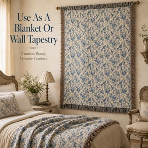 K&ouml;nnte beinhalten: Eine cremefarbene Decke oder Wandteppich mit blauem Blumen- und Vogelmuster. Der Stoff hat einen Fransenrand und wird an einer Wand und auf einem Bett gezeigt. Der Text lautet: "Use As A Blanket Or Wall Tapestry".