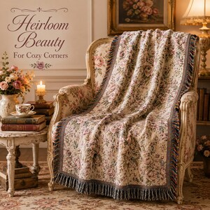 May include: A floral patterned throw blanket draped over a vintage armchair. The blanket features a cream background with pink and green floral designs, a brown border, and fringe. The text "Heirloom Beauty For Cozy Corners" is visible.