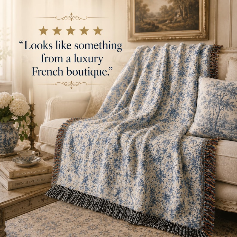 K&ouml;nnte beinhalten: Eine cremefarbene Decke mit blauem Blumenmuster und schwarzem Fransen ist &uuml;ber ein Sofa drapiert. Ein passendes Kissen mit Baumdesign liegt auf dem Sofa. Der Text im Bild lautet: &bdquo;Sieht aus wie etwas aus einer luxuri&ouml;sen franz&ouml;sischen Boutique.&ldquo;