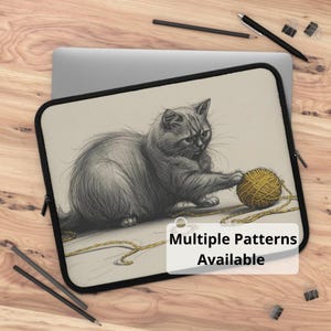 Könnte beinhalten: Laptoptasche mit einer Bleistiftskizze einer grauen Katze, die mit einem gelben Wollknäuel spielt. Die Tasche hat einen schwarzen Rand und einen Reißverschluss. Der Text auf dem Bild lautet "Multiple Patterns Available".