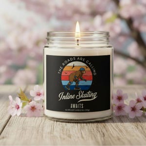 May include: A lit soy candle in a glass jar with a black label. The label features a bear rollerblading with the text "The Roads Are Calling" and "Inline Skating Awaits". The candle is 9 oz (255g) and has a 40-hour burn time.
