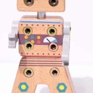 Op de afbeelding: Houten robotspeelgoed met een lichtbruine afwerking en kleurrijke accenten. De robot heeft een hoofd, lichaam en benen die met metalen schroeven zijn verbonden. Het lichaam heeft een paarse streep met kleurrijke cirkels en een meter. De benen hebben een geometrisch ontwerp.