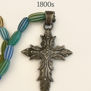 May include: An antique Native American trade cross with trade beads, dating from the 1800s. The cross is made of dark metal with floral detailing. The beads are striped in green, blue, and white.