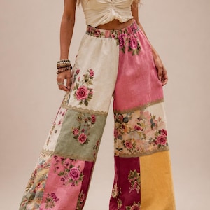 Op de afbeelding: Patchwork broek met wijde pijpen met een rozenpatroon in roze, groen, crème en geel. De broek wordt gecombineerd met een crèmekleurige, geplooid crop top. De stijl is bohemien.