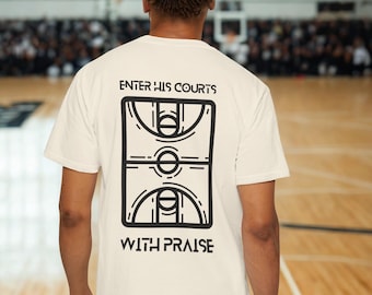May include: Cream-colored t-shirt with a black basketball court graphic and the text "ENTER HIS COURTS WITH PRAISE." The shirt is made of a soft material and is suitable for casual wear. The design is centered on the back of the shirt.