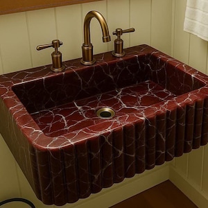 Puede incluir: Un lavabo rectangular montado en la pared con una rica apariencia de m&aacute;rmol rojo y vetas blancas. El lavabo tiene un dise&ntilde;o acanalado en la parte delantera y los lados. Cuenta con un grifo y manijas de bronce.