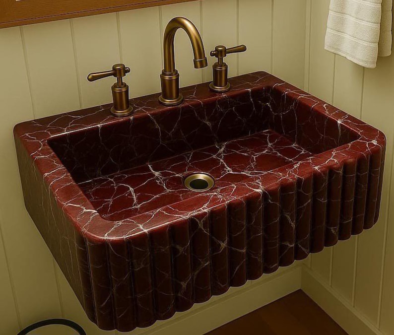 Puede incluir: Un lavabo rectangular montado en la pared con una rica apariencia de m&aacute;rmol rojo y vetas blancas. El lavabo tiene un dise&ntilde;o acanalado en la parte delantera y los lados. Cuenta con un grifo y manijas de bronce.