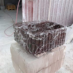 Puede incluir: Un lavabo rectangular de m&aacute;rmol marr&oacute;n oscuro con vetas blancas, apoyado sobre una base de piedra marr&oacute;n claro. El lavabo tiene un exterior texturizado y acanalado. El dise&ntilde;o general sugiere un enfoque en los accesorios de ba&ntilde;o.