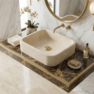 May include: A square beige stone vessel sink with rounded corners and a gold-toned drain, mounted on a dark brown marble countertop with a gold metal edge. The sink features a gold-toned faucet and is positioned in a bathroom with marble walls.