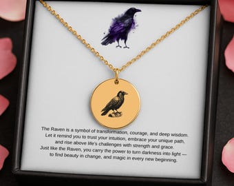 May include: Gold-colored necklace with a round pendant featuring a raven illustration. The necklace is presented in a black box with text about the raven's symbolism. A watercolor-style raven is also depicted above the pendant.