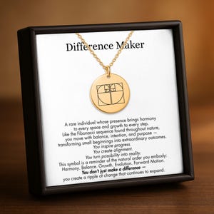 May include: A gold pendant necklace with a circular charm displaying a Fibonacci sequence design. The necklace is in a black box with the words "Difference Maker" and inspirational text.