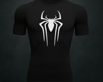 Puede incluir: Camiseta de compresión negra de manga corta con un emblema de araña blanco en el pecho. La camiseta deportiva tiene cuello redondo y mangas raglán. El logotipo de la araña es un diseño estilizado y simétrico.